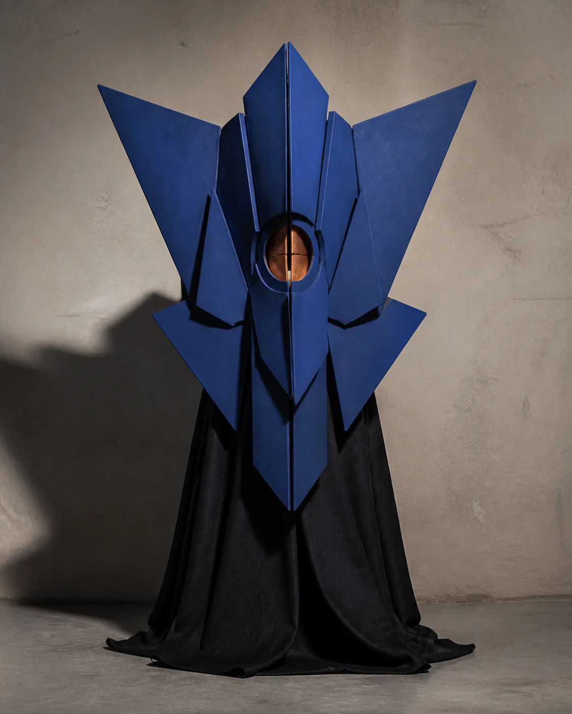CALYX as a cobalt arrangement of ceramic planes around one copper aperture above a black mantle.